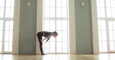 Yoga yapan esnek bir kız, geniş pencerenin yanındaki ışık sınıfında asma dansı yapıyor..