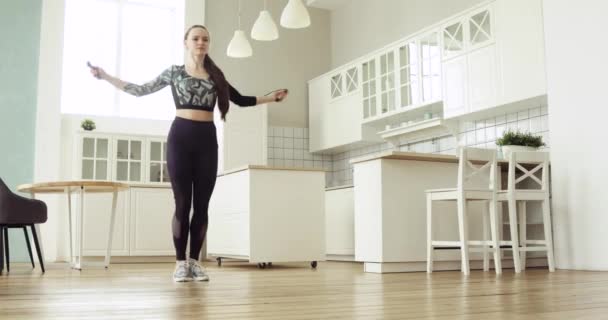 Νεαρή σπορ γυναίκα πηδάει σχοινί κάνοντας καρδιο κατάρτισης στο σπίτι στην κουζίνα. — Αρχείο Βίντεο