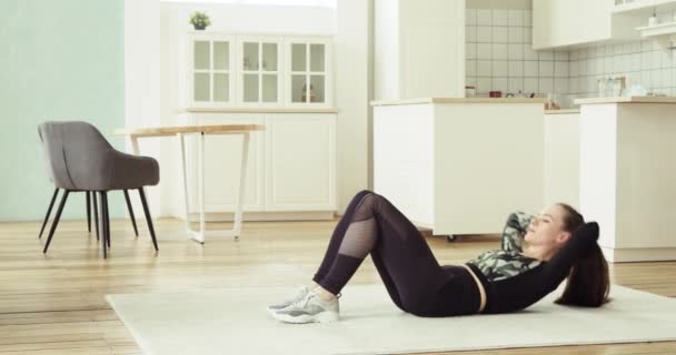 Νεαρή γυναίκα κάνει κοιλιακές ασκήσεις crunches στο πάτωμα στο σπίτι, πλευρική άποψη. — Αρχείο Βίντεο