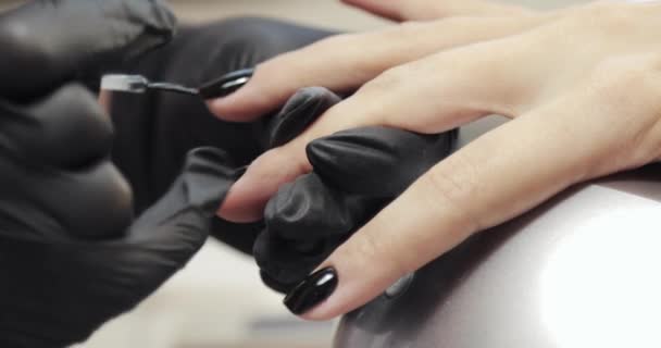 Мастер маникюра покрытия клиентов картины ногти черный шеллак, руки крупным планом . — стоковое видео