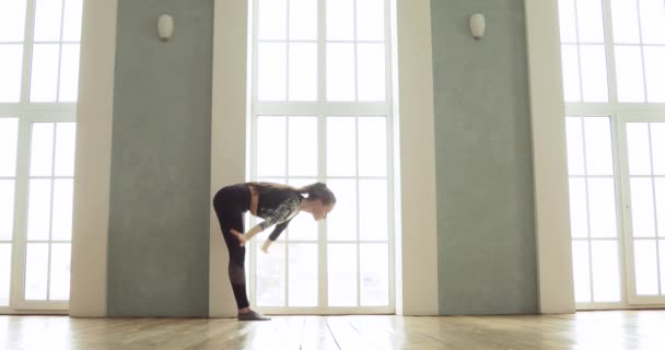 Flexibel tjej utövar yoga utför asanas i lätt klass nära stora fönster. — Stockvideo