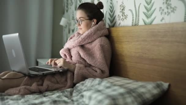 ラップトップノートパソコンを使ってベッドに横になっている若い女性は、画面入力メッセージ、ウェブカメラのビデオ通話、コンピュータの閲覧中のチャットインターネットソーシャルメディアの勉強や自宅でオンラインで働く — ストック動画