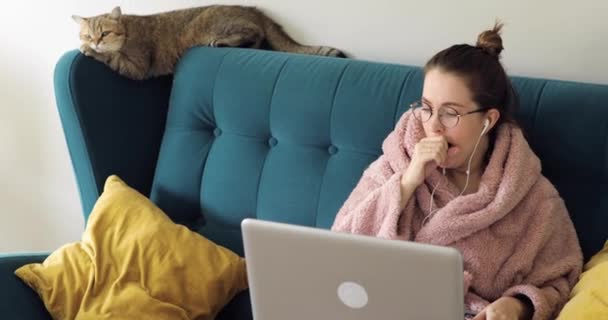 Genç bir kadın dizüstü bilgisayar kullanarak kanepede oturuyor, ekran daktilo mesajlarına bakıyor, web kamerası görüntülerine bakıyor, internette sohbet ediyor, internette geziniyor, sosyal medyada çalışıyor ya da evde çalışıyor. — Stok video