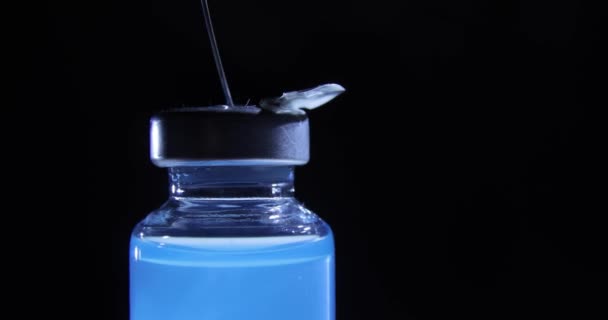 Dials blue coronavirus vaccine into syringe on black background, closeup view. — Stock Video