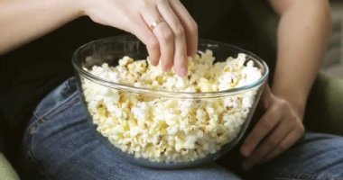 Kadın cam kaseden patlamış mısır yiyor. Dizlerinin üzerinde, elleri yakın..