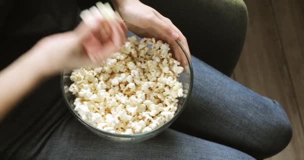 Kobieta je popcorn ze szklanej przezroczystej miski na kolanach, ręce zbliżenie. — Wideo stockowe