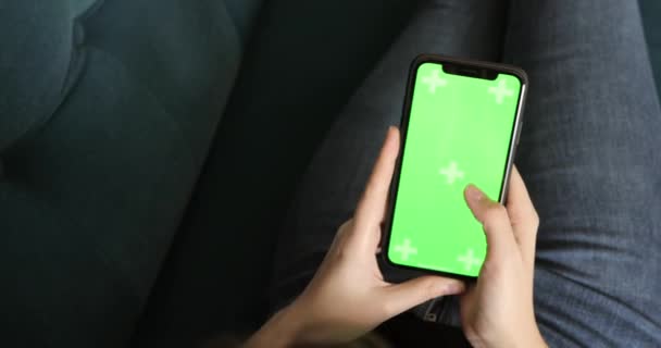 Ung flicka bläddrar smartphone med grön skärm ligger på soffan, närbild. — Stockvideo