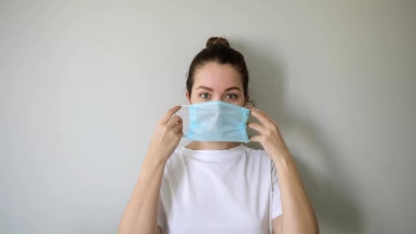 Woman is putting on mask on face in coronavirus pandemic on grey background. — Stock Video