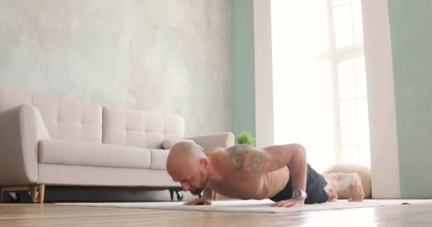 Atletische jonge shirtloze man in korte broek doet push-ups in de woonkamer thuis. — Stockvideo