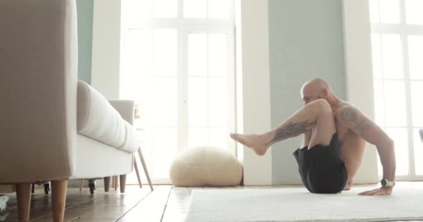 Atletische man doet buikspieroefeningen thuis trekt zijn benen tegen de borst. — Stockvideo