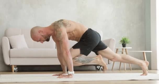 Atletische man in korte broek is het trainen en doen van dynamische oefeningen in plank thuis. — Stockvideo