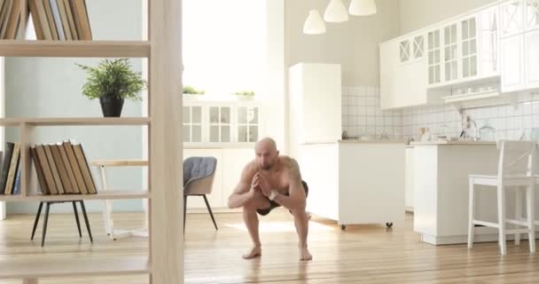 Musculoso hombre sin camisa está haciendo sentadillas con saltos en el entrenamiento de cocina en casa . — Vídeos de Stock