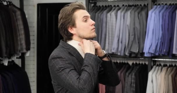 Jeune homme essaie costume élégant avec chemise en magasin et en regardant miroir . — Video