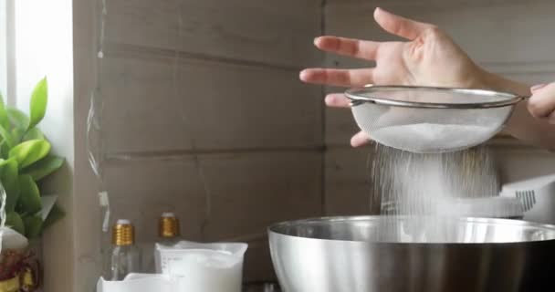 Woman sifting flour through sieve for baking, mixing ingredients in metal bowl. — Stock Video