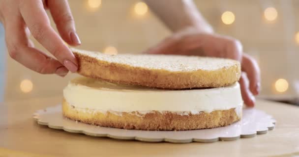 Suikerspin vrouw is het zetten van spons cake op room maken taart, handen closeup. — Stockvideo