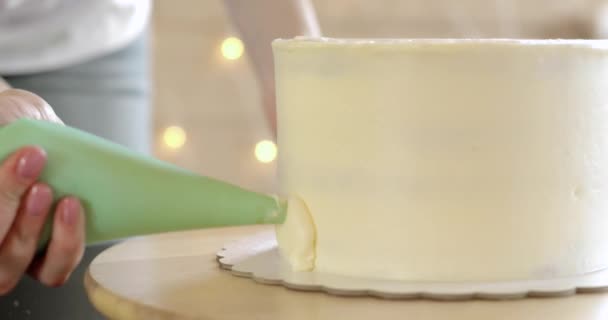 Banketbakker gieten crème aan de zijkanten van taart top jas met behulp van gebak zak, close-up. — Stockvideo