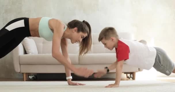 Entrenamiento familiar de mamá e hijo haciendo ejercicio de tablón en casa dando cinco . — Vídeo de stock