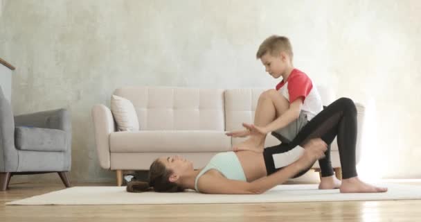 Mãe mulher fazendo glute ponte exercício de treino com filho sobre ela como haltere . — Vídeo de Stock