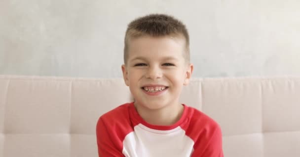 Portret van kleine lachende jongen zit op de bank en kijkt naar de camera. — Stockvideo