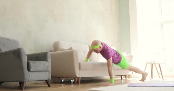 Homem de sportswear brilhante está fazendo exercícios push-ups usando sofá em casa . — Vídeo de Stock