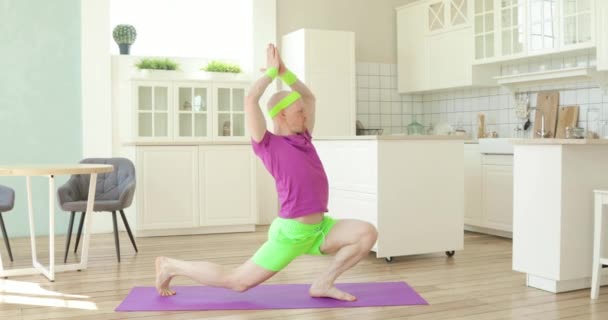 Funny man is doing yoga warrior pose asana on mat in kitchen, sportive humor. — Stock Video