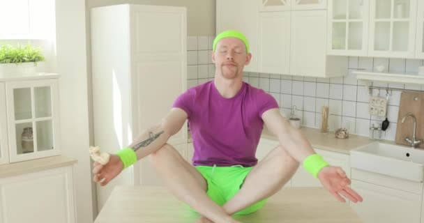 Homem está praticando meditação em pose de ioga de lótus na cozinha e comer donoughts . — Vídeo de Stock