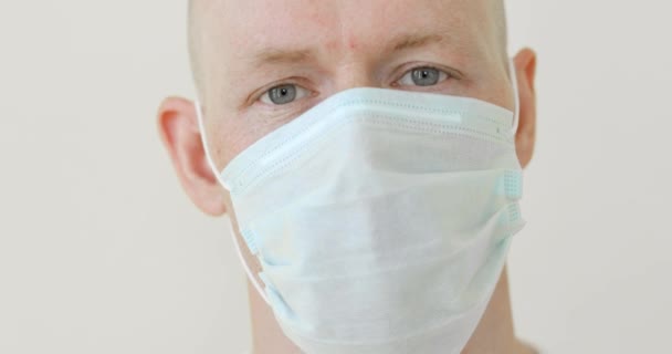 白い背景にコロナウイルスのパンデミックで医療マスクに閉じ込められた男の顔. — ストック動画