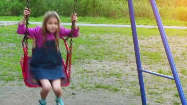 Маленькая красивая девочка едет кататься на качелях в летний городской парк . — стоковое видео