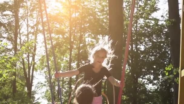 Movimento lento: Duas irmãs montam em um balanço no parque da cidade de verão . — Vídeo de Stock