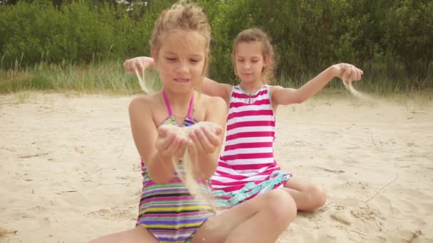 Slow Motion: Two little beautiful girls pour sand on shore of Baltic Sea in Jurmala, Latvia. — Stock Video