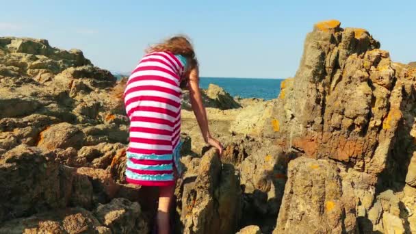 Niña hermosa camina sobre rocas de piedra en la costa mediterránea . — Vídeo de stock