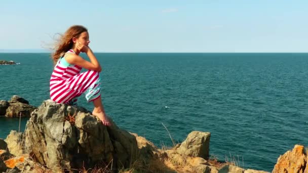 Niña hermosa sentada en la orilla rocosa del mar Mediterráneo . — Vídeos de Stock