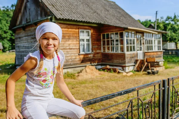Маленькая спокойная девочка в белом шарфе рядом с сельским домом — стоковое фото