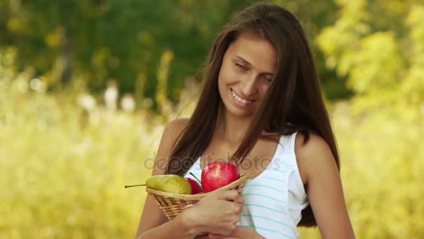 Bella giovane donna che tiene un cesto di frutta e mangia mela nel parco verde estivo della città . — Video Stock