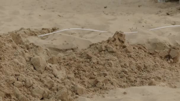 Man graaft schop zand voor het leggen van elektrische kabels. — Stockvideo