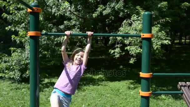 Little girl pulls up on horizontal bar in summer city park. — Stock Video