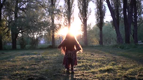 Movimento lento: Menina bonita alegremente pulando no parque da cidade de verão contra o pôr do sol de fundo . — Vídeo de Stock