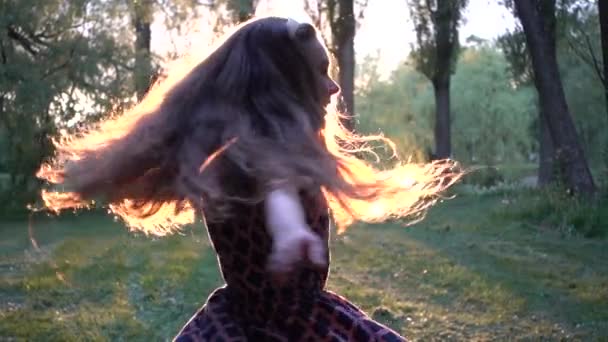 Movimiento lento: Hermosa niña divirtiéndose girando en el parque de la ciudad de verano contra la puesta de sol de fondo . — Vídeo de stock