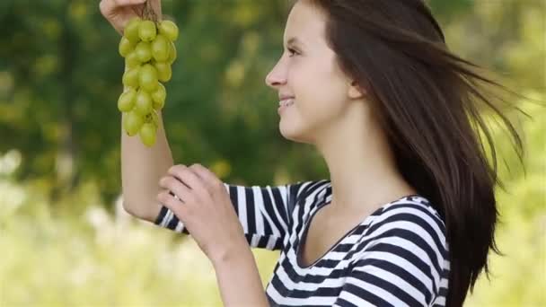 Joven mujer atractiva comiendo uvas, contra verde del parque de verano . — Vídeos de Stock