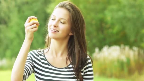 Красивая молодая женщина длинноволосая брюнетка на заднем плане летний парк улыбается держа лимон — стоковое видео