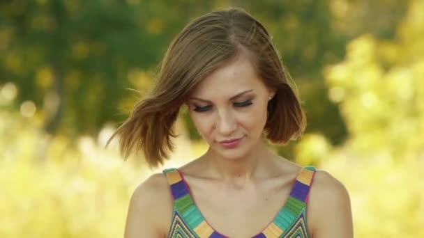 Retrato de una joven hermosa y sonriente de cerca, contra el verde del parque de verano . — Vídeos de Stock