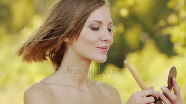 Mladá krásná žena s nahá ramena klade základ na obličej na pozadí zelené letní městský park. — Stock video
