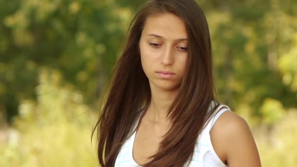 Портрет молодой красивой грустной женщины на фоне зеленого летнего городского парка . — стоковое видео