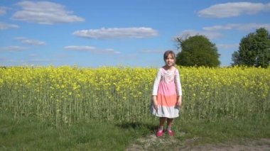 Ağır çekim: güzel küçük kız sarı çiçek açan törpülemek ile yaz alan arka plan karşı neşeyle atlama.