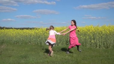 Slow Motion: İki gülen küçük kız kardeş eller katıldı ve sarı çiçek açan törpülemek ile yuvarlak dans yaz alan arka plan karşı çevirdim.