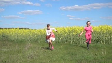 Ağır çekim: İki güzel küçük kız kardeş mutlu yaz alan arka planı sarı çiçek açan törpülemek ile çalıştırın.
