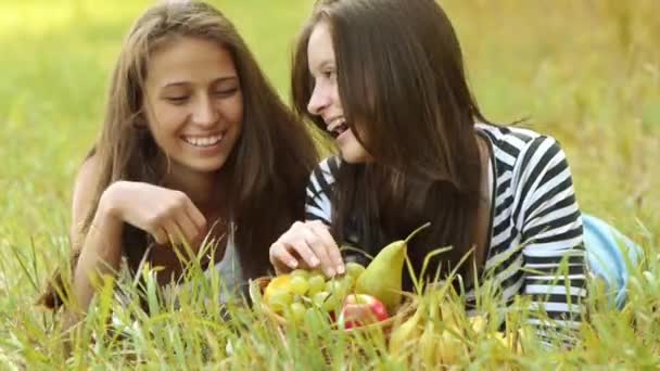 Dos hermosas mujeres jóvenes yacen sobre hierba verde y comen uvas maduras . — Vídeos de Stock