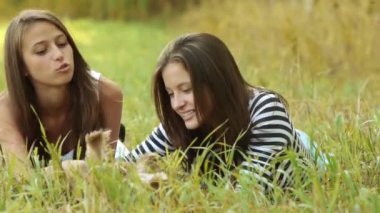 İki güzel genç kadın yeşil çim üzerinde yalan ve küçük tüylü köpek oynamak.