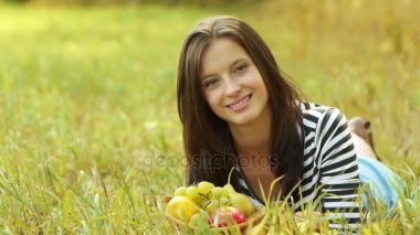 Genç güzel kadın yeşil çimenlerin üzerinde yatıyor ve olgun armut yemek.