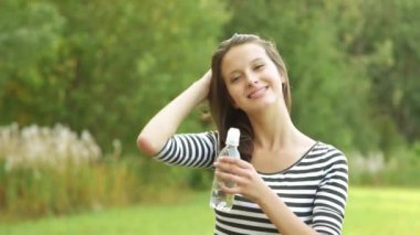 güzel genç kadın çizgili ceket daimi park yaz aylarında suyu şişeden içer.